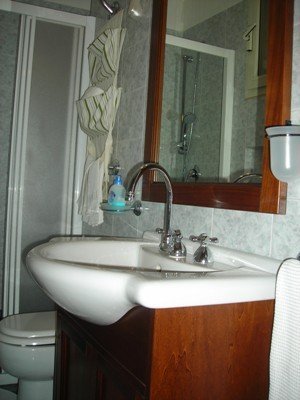 Bagno con apertura, lavabo incassato nel mobiletto in legno, specchio, tazza-bidè,box-doccia, phon e accessori.  