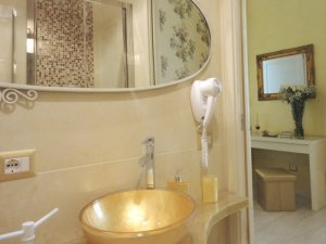 The private bathroom has wall and floor tiles that reproduce the travertine marble, and a sink basin sitting on gold glitter counter